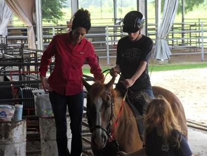 Woman shows boy how to hold the horses reins